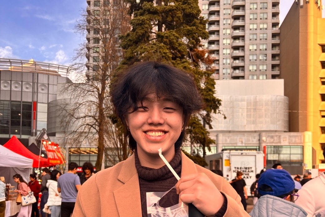 Daniel Park outdoors in a long coat, holding a drink, smiling at the camera