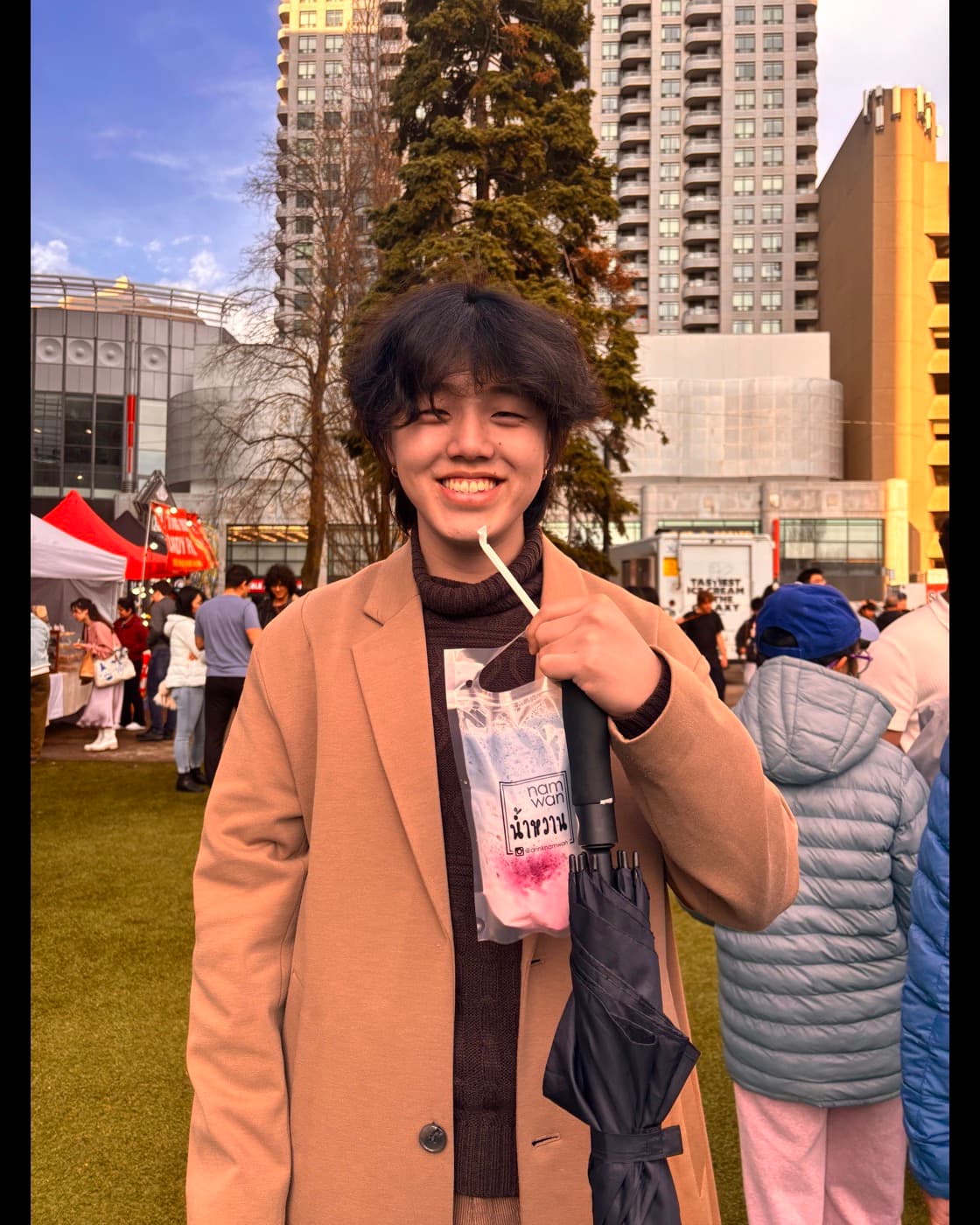 Daniel Park outdoors in a long coat, holding a drink, smiling at the camera